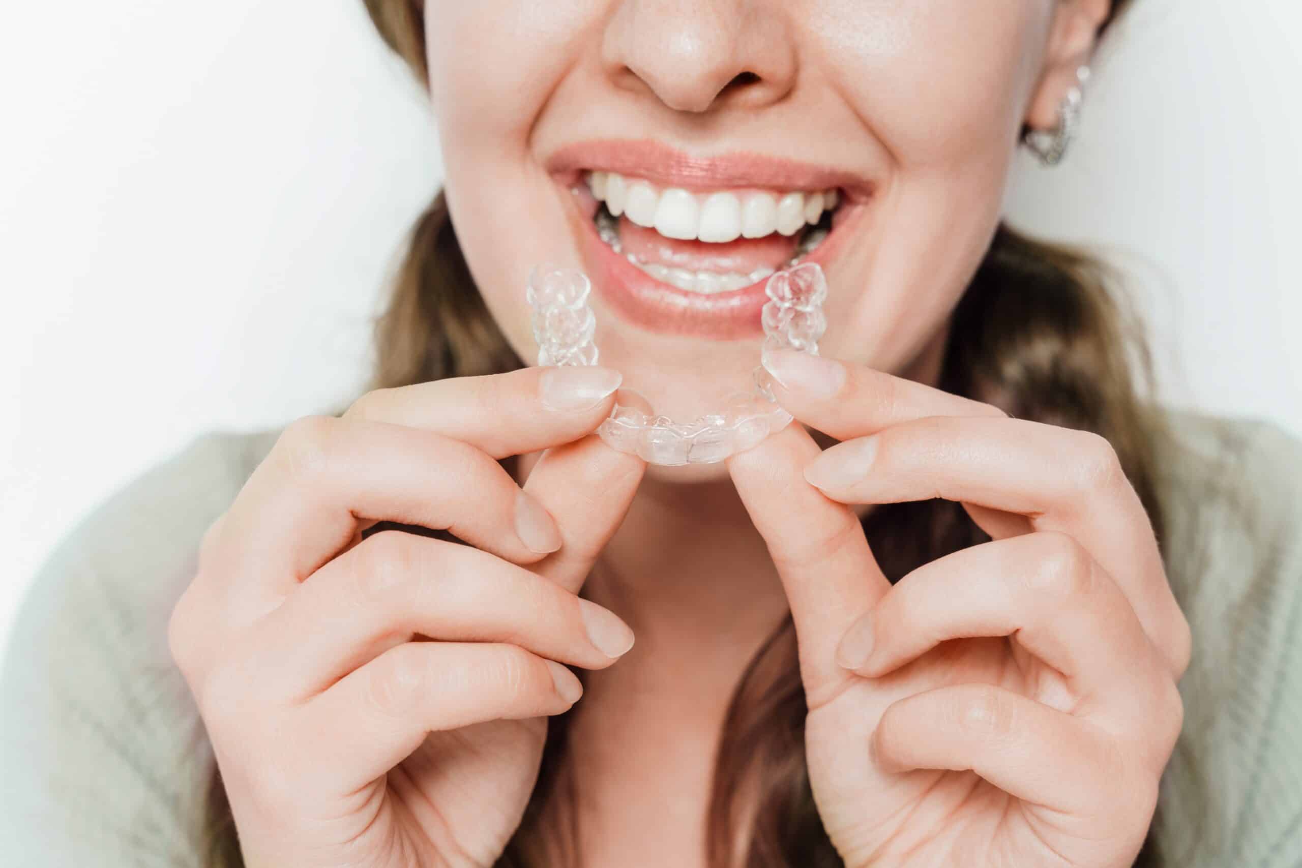 Woman smiling and holding a clear teeth aligner with both hands, dental care and orthodontic treatment aligners