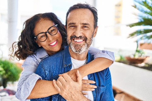 mature couple with their arms around each other, smiling with their new dental veneers