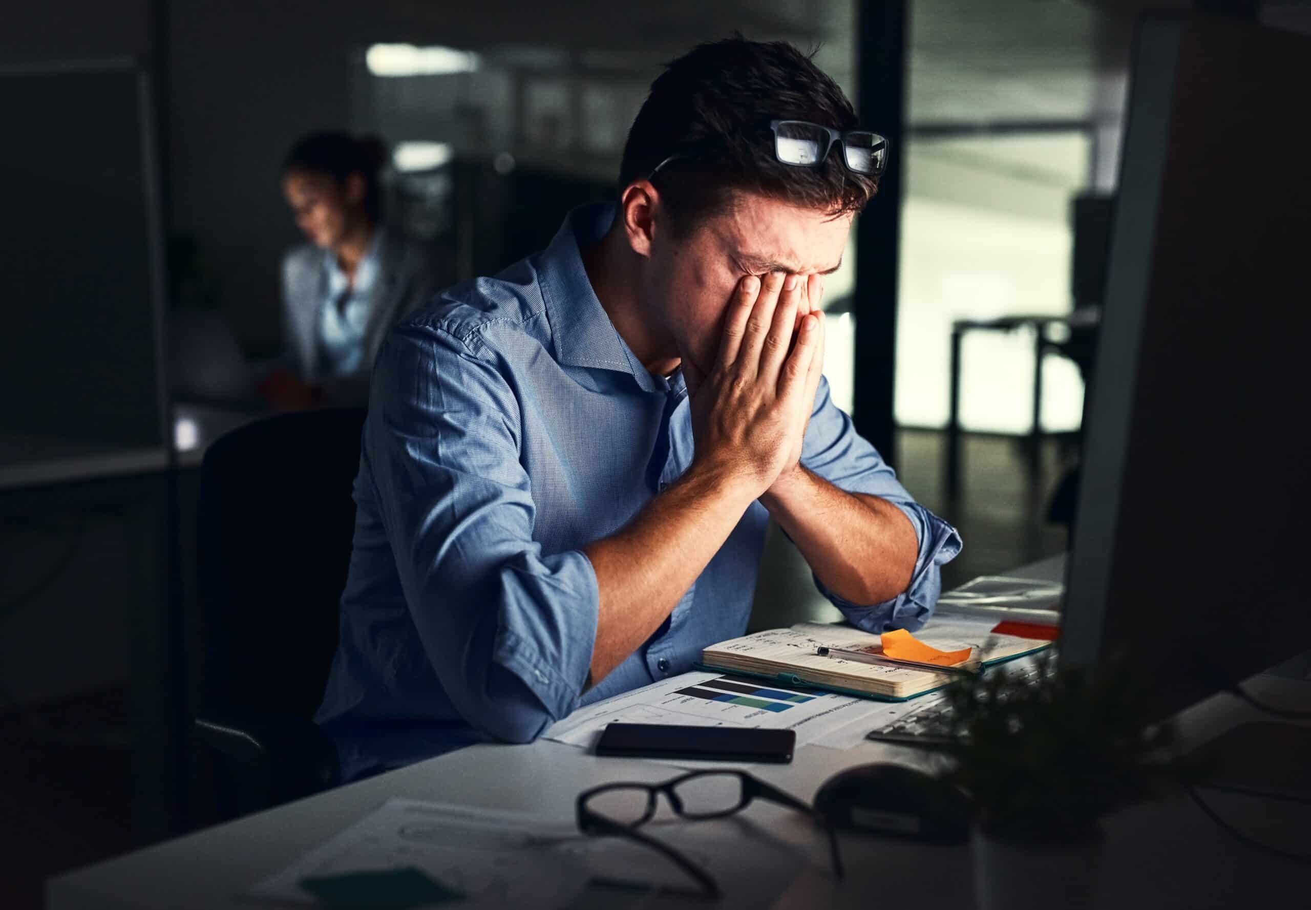 man at his desk with his head in his hands, suffering from sleep problems