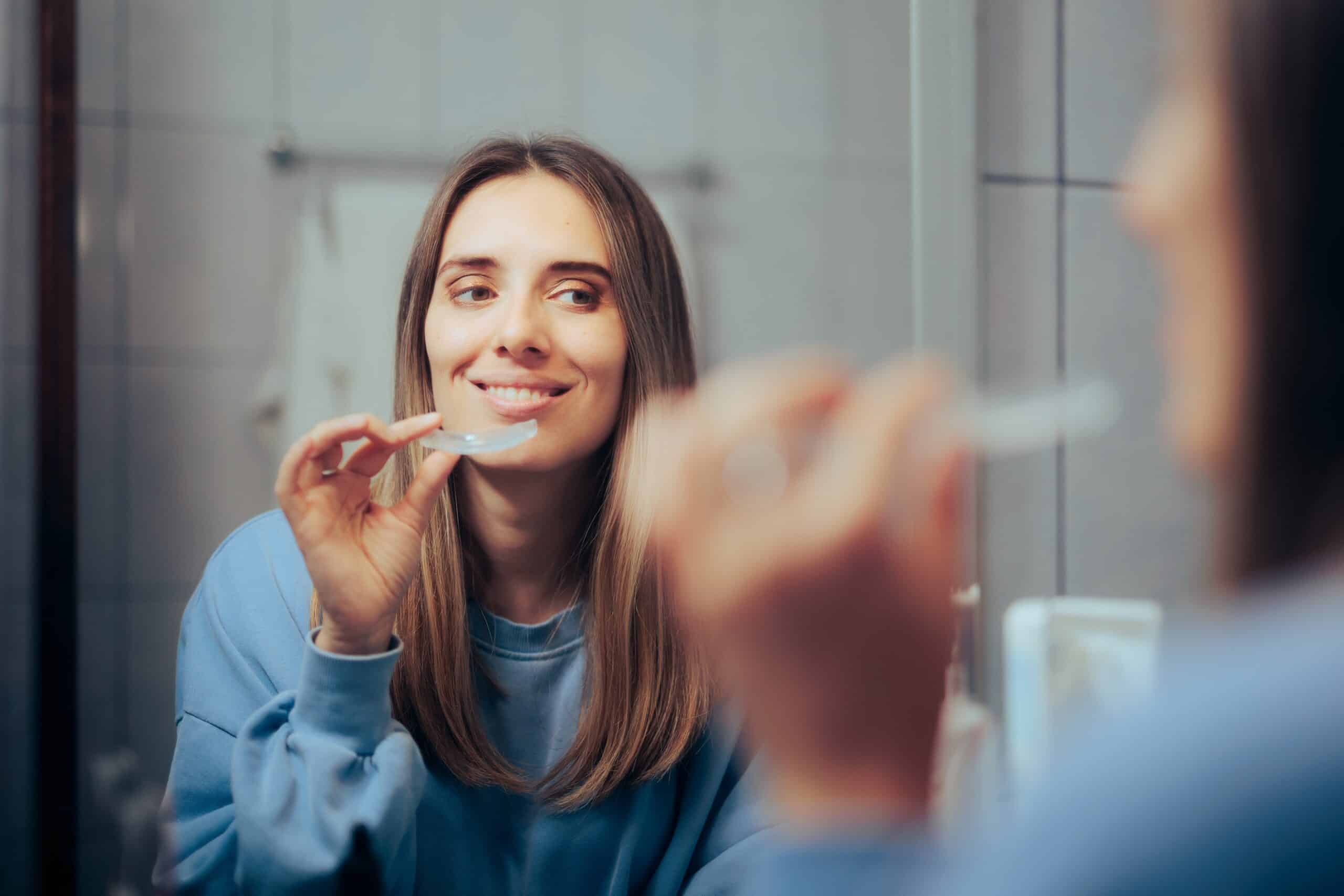 young woman placing her clear aligners in the mirror