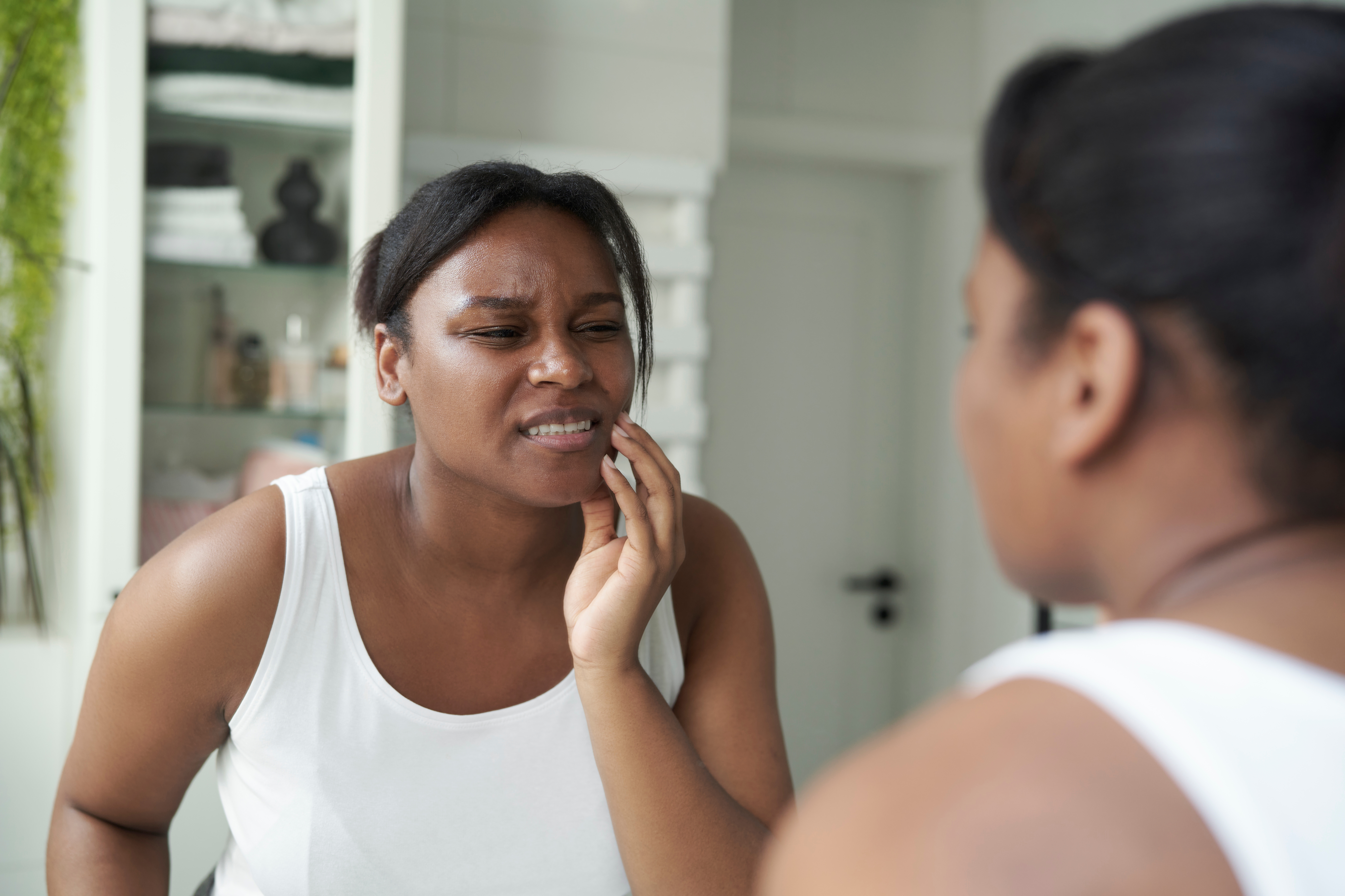 woman looking in mirror holding her jaw, bruxism