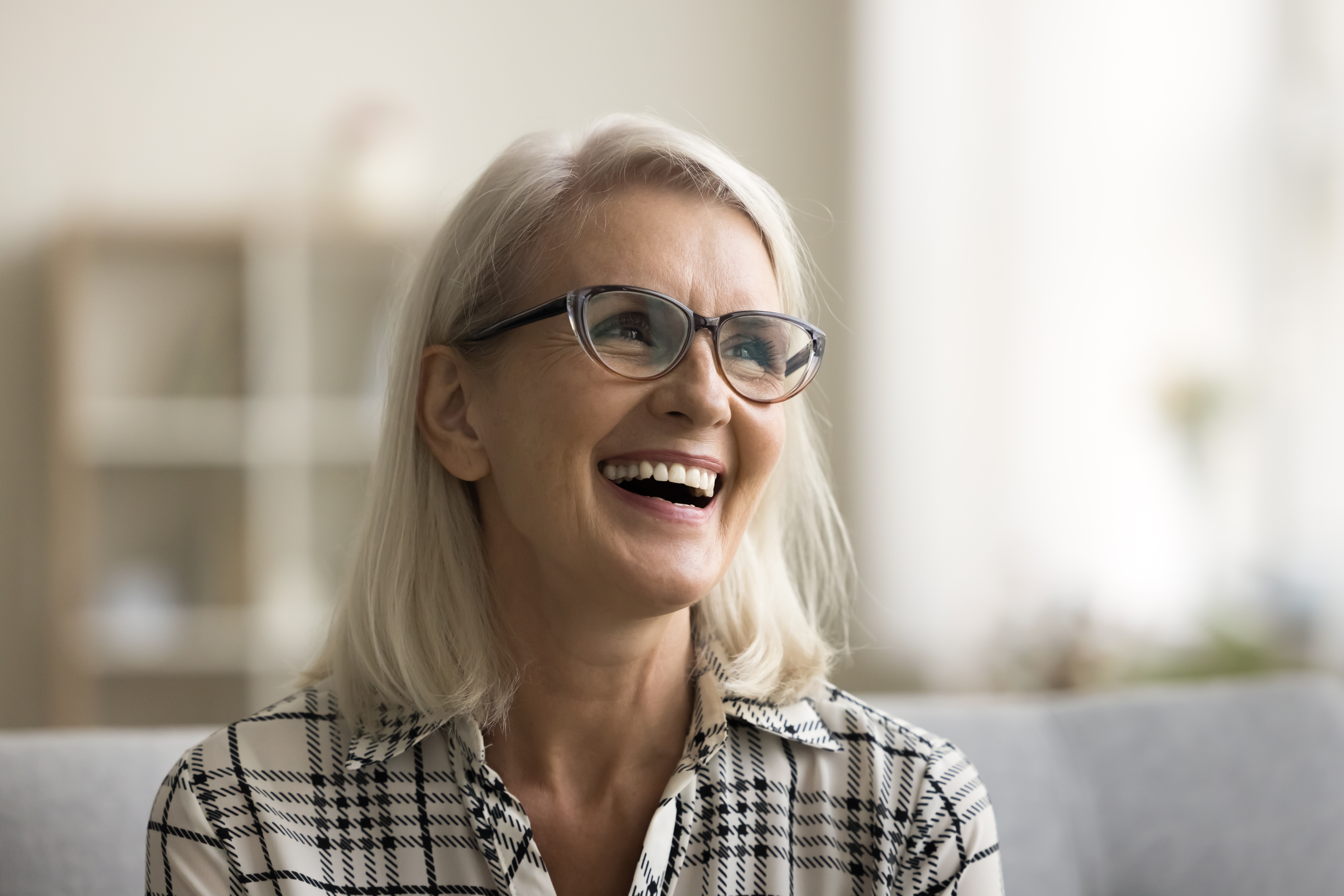 older woman smiling sitting on a couch, new dental implants