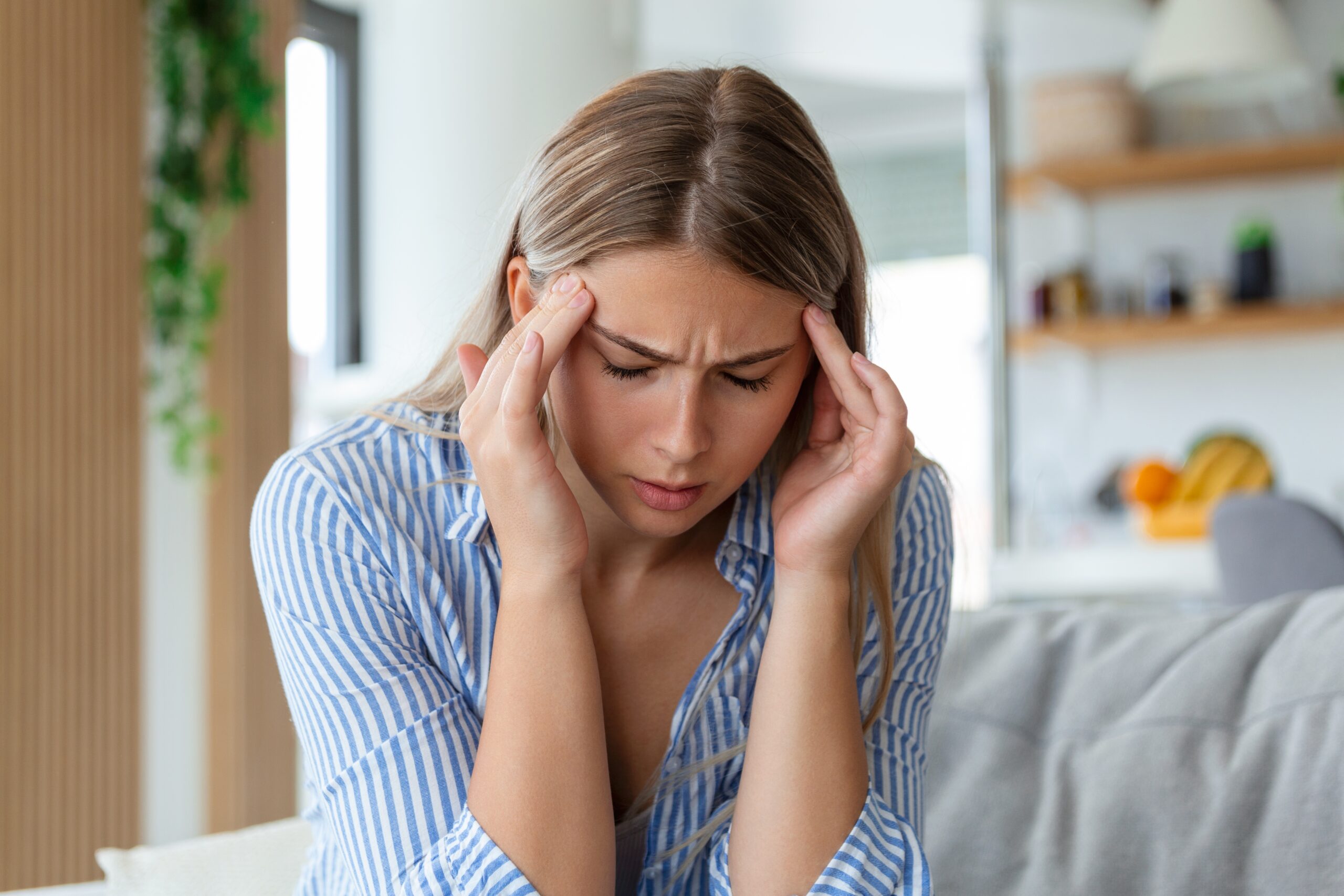 young woman on a couch with a very paintful headache, TMJ pain