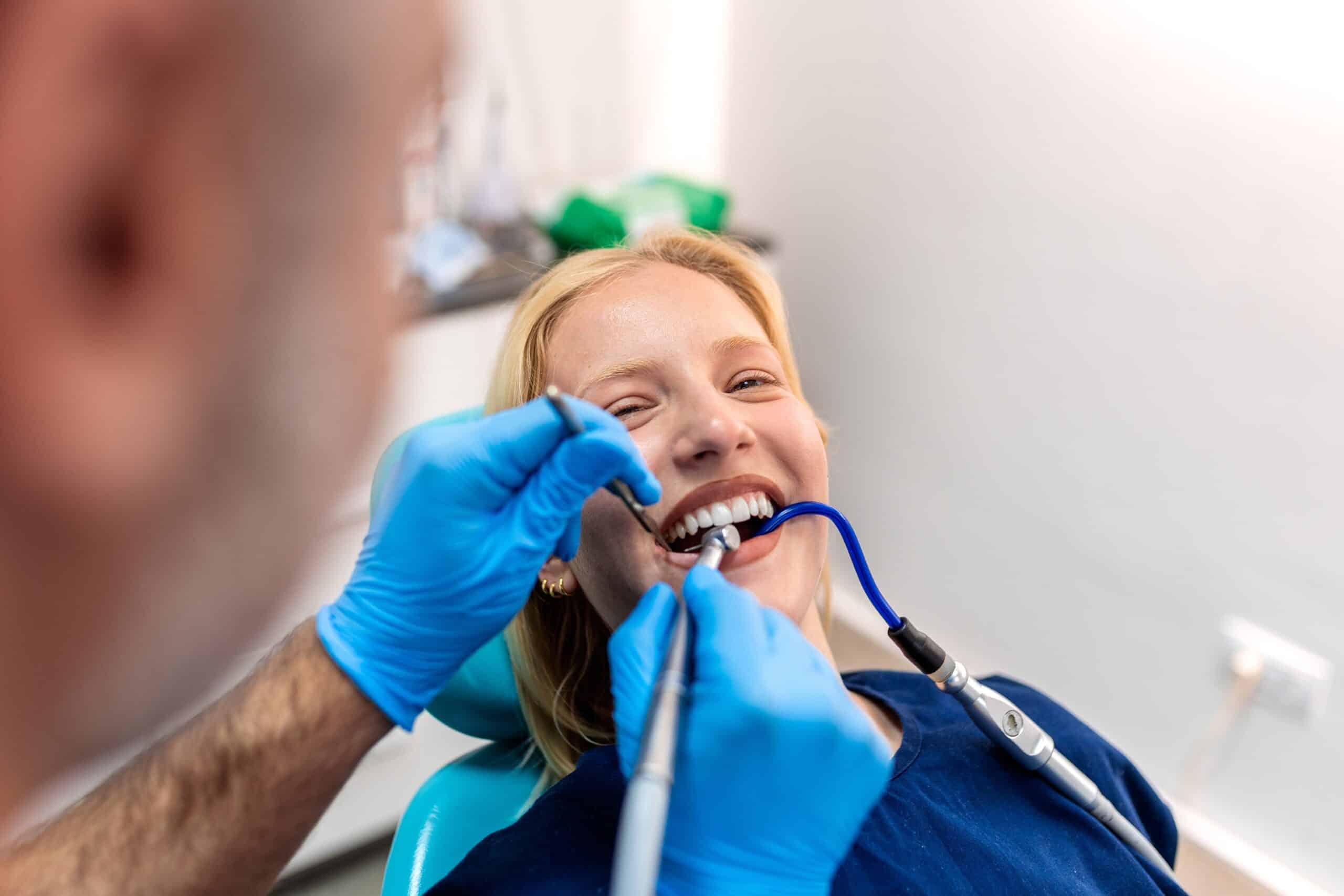 Smiling dentist communicating with young woman while checking her teeth during dental procedure