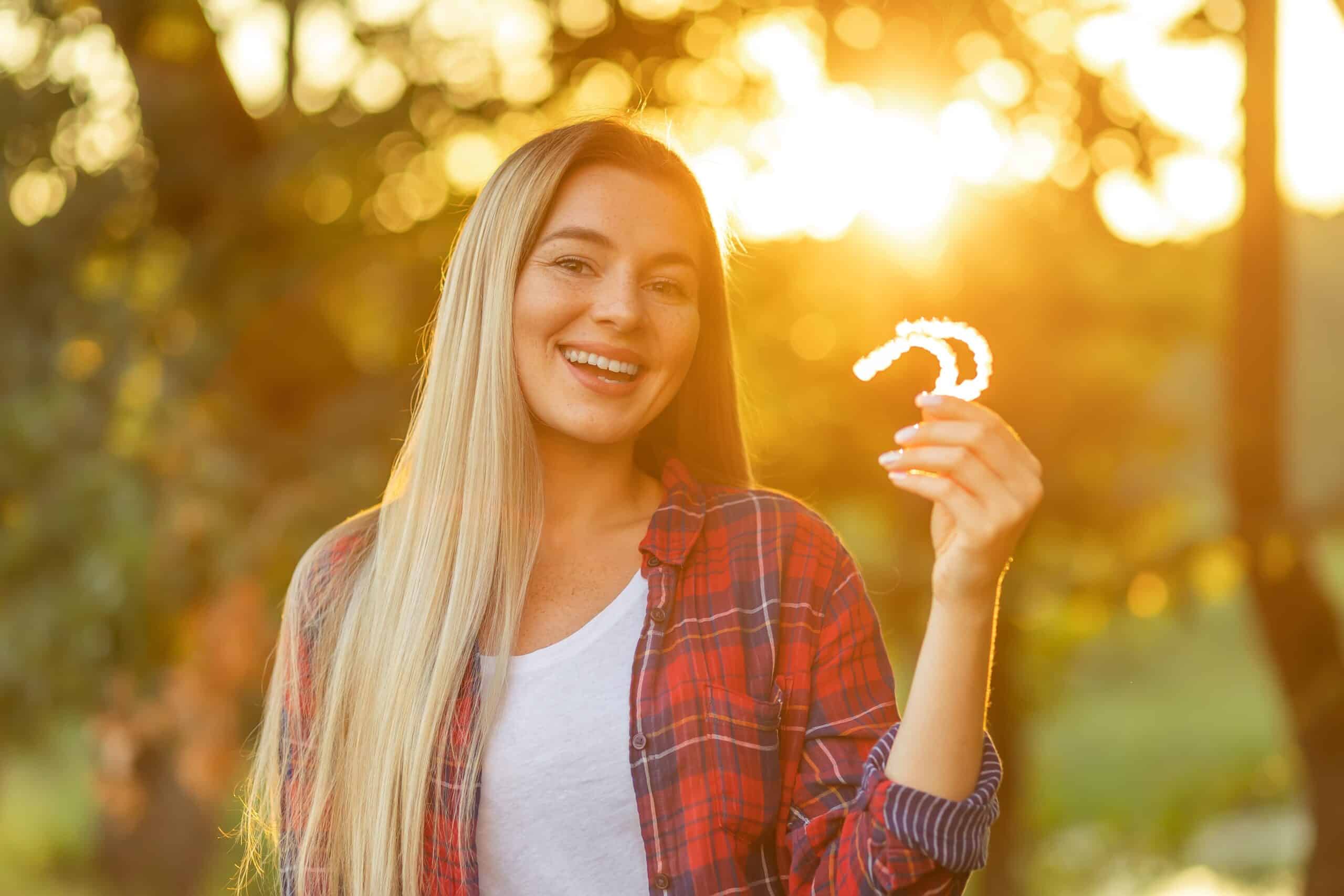 young woman smiling outdoors at sunset, holding up her clear aligners
