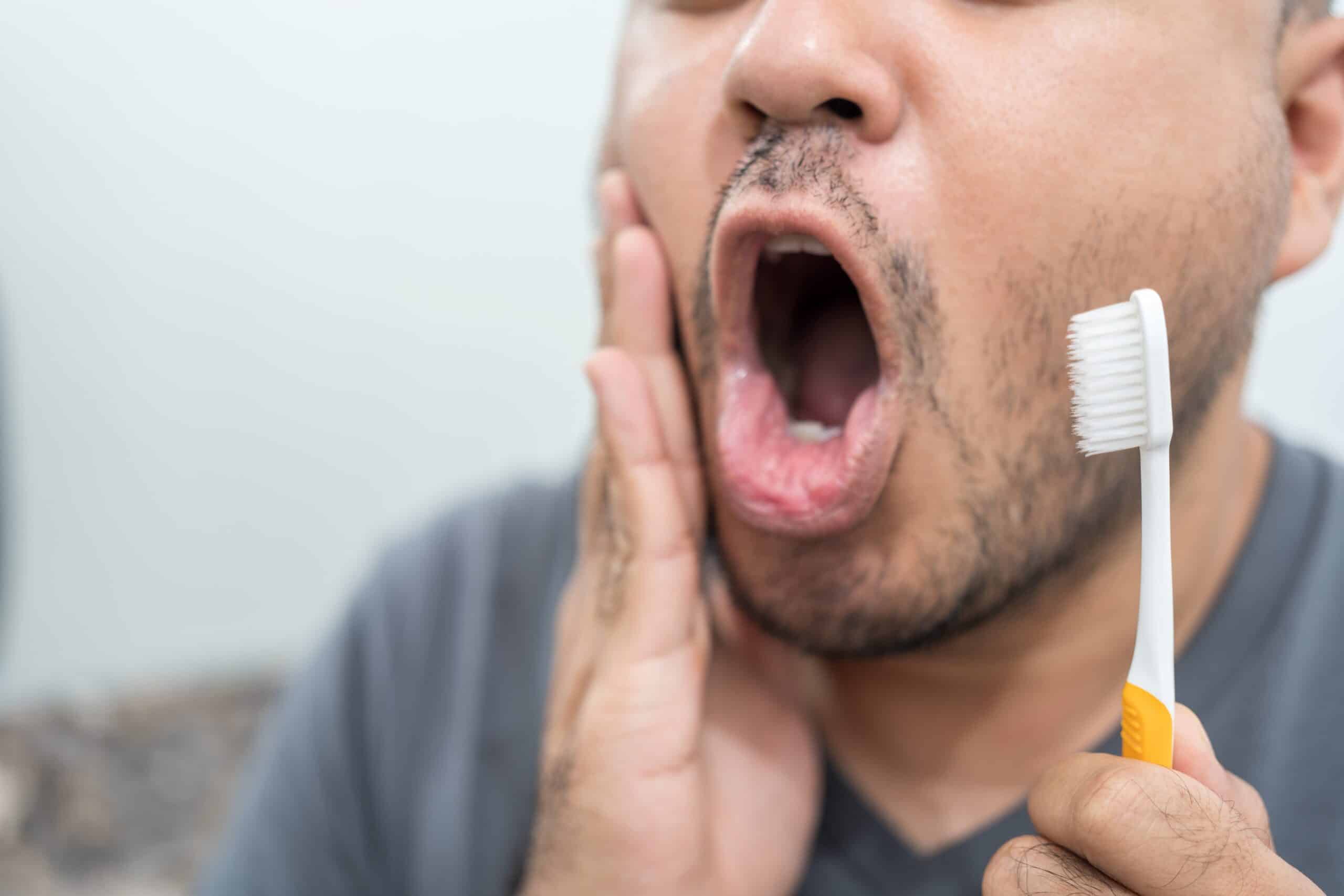 man brushing his teeth experiencing tooth pain
